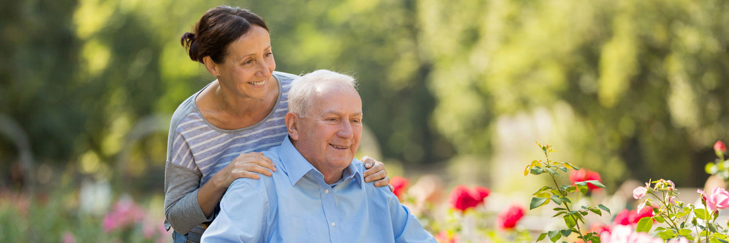 caregiver and elderly man outside surrounded by flowers